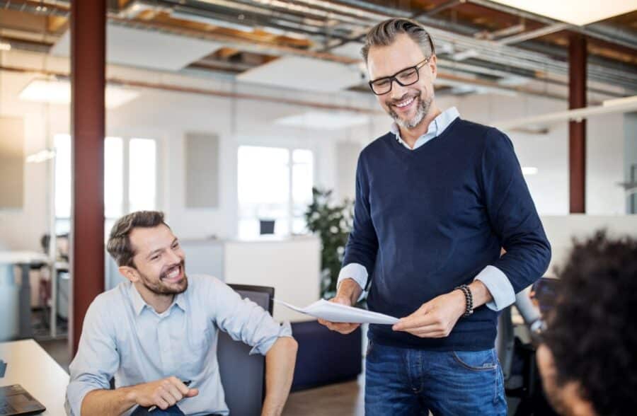 Zwei lachende Männer im Büro; einer hält den Bauvertrag in der Hand© gettyimages/Luis Alvarez