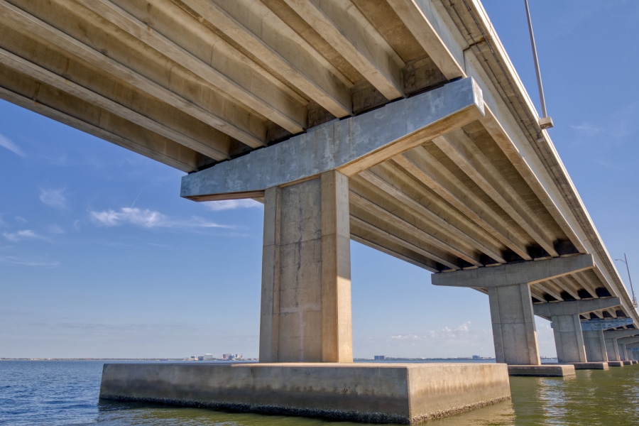 View of the Howard Frankland Bridge from underneath, showcasing its sturdy concrete pillars and expansive span over Tampa Bay, symbolizing modern infrastructure and engineering.