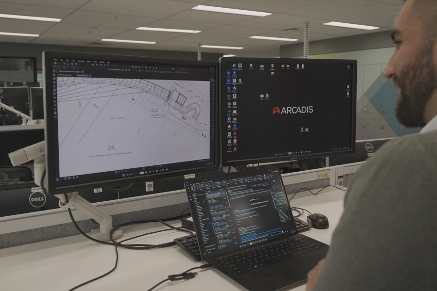 Engineer working at a dual-monitor workstation displaying detailed infrastructure plans and Arcadis software, emphasizing digital tools in modern construction project management.