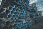 Steel pipes stacked in a warehouse, representing the construction industry's reliance on steel materials. The image reflects the impact of the blocked U.S. Steel merger on construction projects in 2025, highlighting the challenges posed by rising steel costs and supply chain disruptions in the industry.