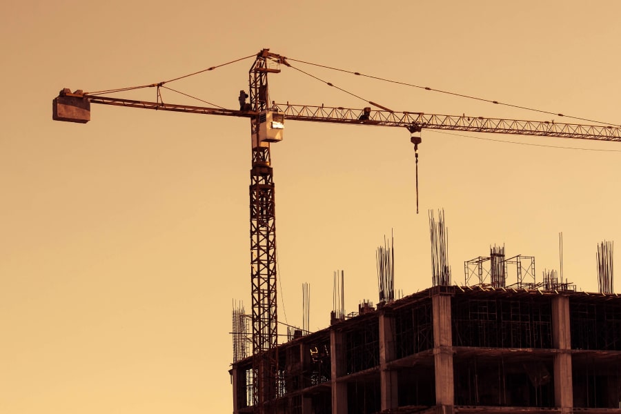 A silhouetted construction crane and partially built structure stand against a golden sunset, symbolizing the construction industry's challenges and transformations. The image conveys resilience and progress, fitting for the topic of how immigration and tariff policies impact the construction sector.