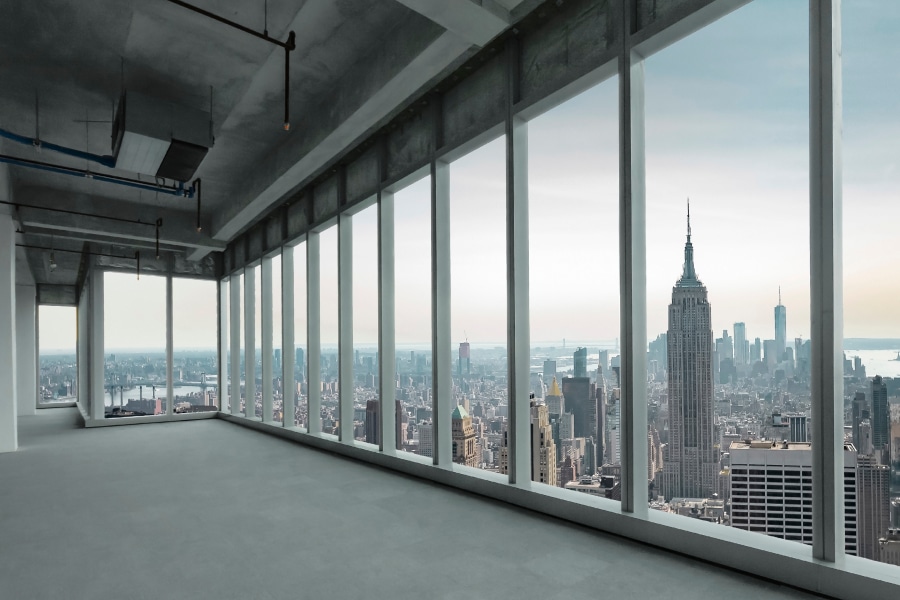 A spacious, unfinished high-rise office with floor-to-ceiling windows overlooking the New York City skyline, including the Empire State Building. The modern, open-floor space reflects the growing demand for premium office real estate, highlighting the opportunities for AEC leaders in the evolving high-end office market.