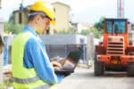 Construction engineer using a laptop at a job site, showcasing the role of digital technology and open data standards in modern infrastructure projects. The future of infrastructure tech relies on seamless data integration for improved collaboration and efficiency.