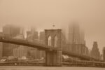 Sepia-toned image of the Brooklyn Bridge enveloped in fog, with the New York City skyline in the background. The bridge, completed under the leadership of Emily Warren Roebling, stands as a testament to her pivotal role in its construction.