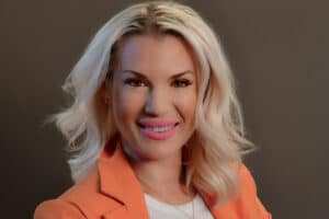 Portrait of Jessica Bjork-Madrigal, VP and Co-owner of Bjork Construction, smiling in a professional setting. She is dressed in an orange blazer, showcasing her leadership and commitment to integrity in the construction industry