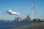 Wind turbines and oil refinery near water under blue sky—symbolizing the oil and gas industry’s transition to sustainable energy through digital collaboration.