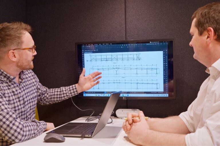 Two engineers review structural design drawings on a monitor using Bluebeam software during a collaborative meeting at Pinnacle Engineering.
