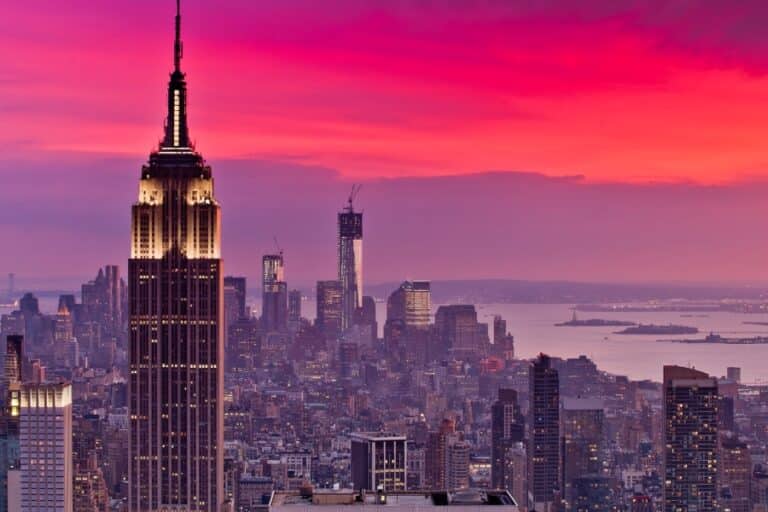 A dramatic sunset over Manhattan highlights the Empire State Building and One World Trade Center—two iconic symbols of American resilience, innovation, and ambition—representing megaprojects that shaped U.S. infrastructure and identity.