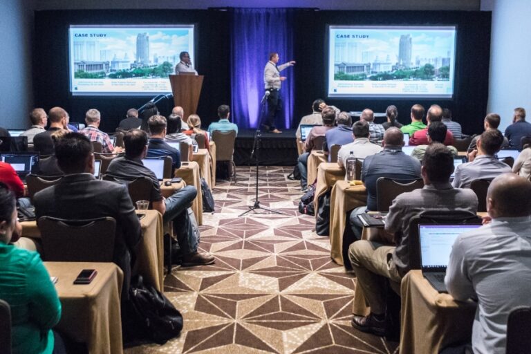 Attendees at a Bluebeam Unbound conference session watch a case study presentation in a packed room with laptops open, highlighting key sessions and industry insights.