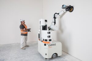 Construction worker operates the Canvas 1200CX drywall robot, which autonomously tapes, muds, and sands a wall surface without blueprints or scans, streamlining interior finishing work on a modern jobsite.