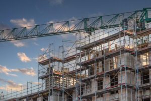 Scaffolding and a tower crane surround a mid-rise apartment building under construction in Germany, symbolizing the country’s stalled construction industry in 2025 amid soaring costs, higher mortgage rates, and shrinking housing permits.