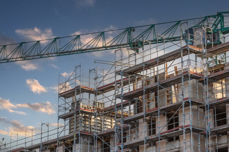 Scaffolding and a tower crane surround a mid-rise apartment building under construction in Germany, symbolizing the country’s stalled construction industry in 2025 amid soaring costs, higher mortgage rates, and shrinking housing permits.