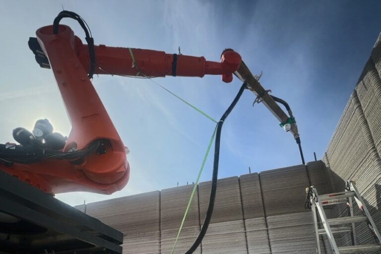Robotic 3D printer RIC-PRIMUS pouring concrete walls for a big-box retail store under blue sky, demonstrating how construction robots cut labor and build time to finish warehouses in just seven days.