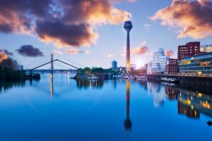 Düsseldorf skyline at sunset with the Rheinturm tower and Medienhafen Gehry buildings reflected in the harbor