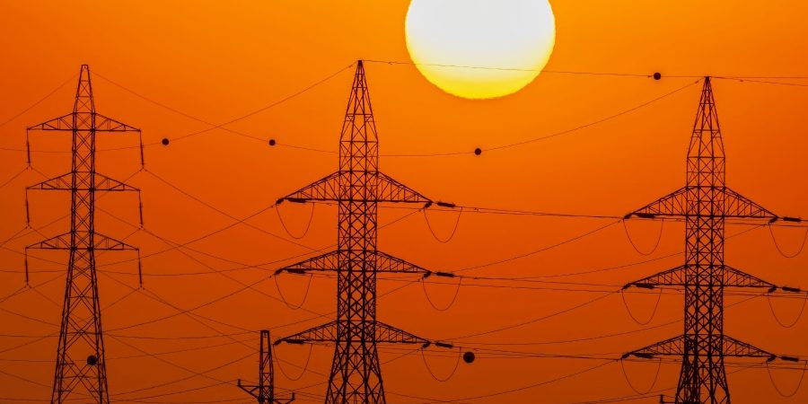 High-voltage power transmission towers silhouetted against the sun, illustrating how AI-driven demand is stressing U.S. power grid infrastructure and exposing permitting delays.