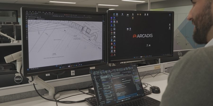 Engineer working at a dual-monitor workstation displaying detailed infrastructure plans and Arcadis software, emphasizing digital tools in modern construction project management.