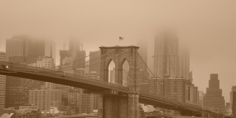 Sepia-toned image of the Brooklyn Bridge enveloped in fog, with the New York City skyline in the background. The bridge, completed under the leadership of Emily Warren Roebling, stands as a testament to her pivotal role in its construction.