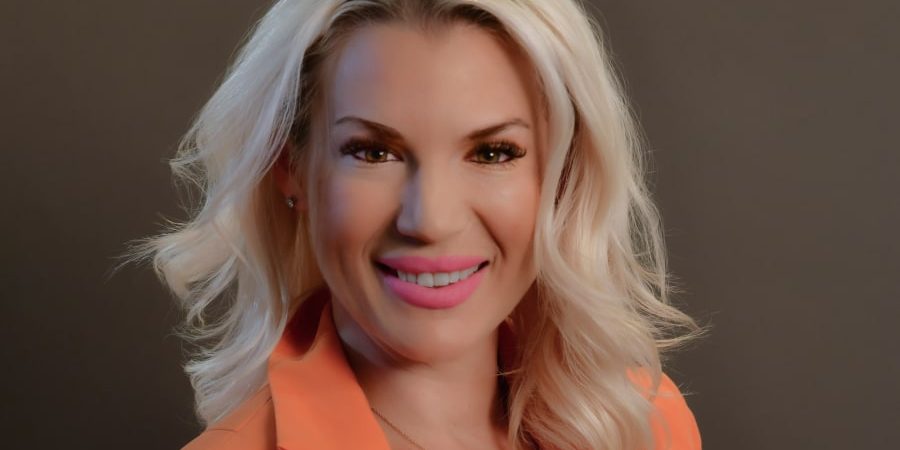 Portrait of Jessica Bjork-Madrigal, VP and Co-owner of Bjork Construction, smiling in a professional setting. She is dressed in an orange blazer, showcasing her leadership and commitment to integrity in the construction industry