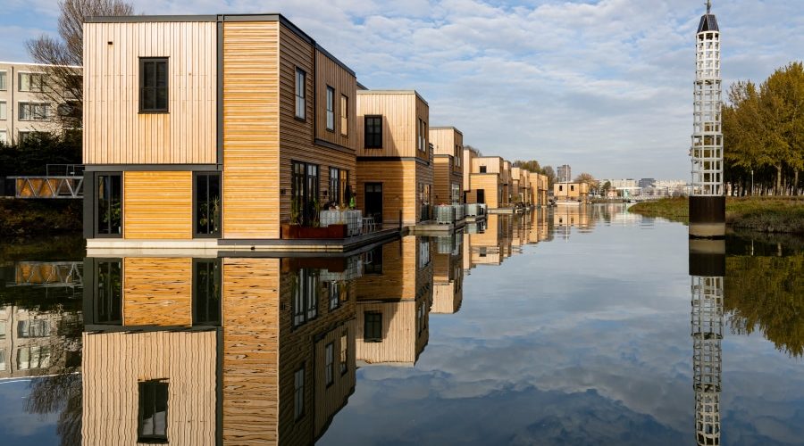 Modern floating homes with sustainable wooden exteriors reflecting on calm water in an urban canal, showcasing innovative floating architecture as a solution to urban space challenges.