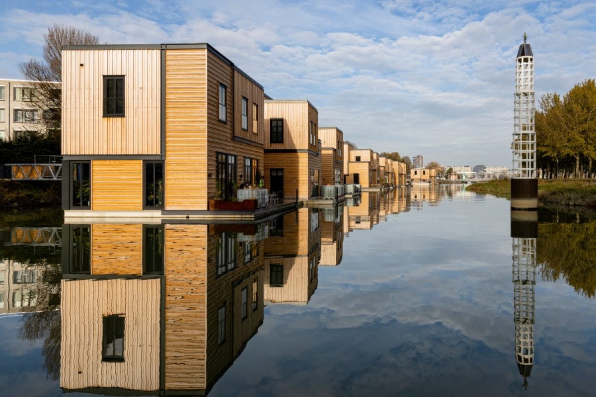 Modern floating homes with sustainable wooden exteriors reflecting on calm water in an urban canal, showcasing innovative floating architecture as a solution to urban space challenges.