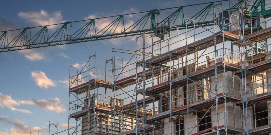 Scaffolding and a tower crane surround a mid-rise apartment building under construction in Germany, symbolizing the country’s stalled construction industry in 2025 amid soaring costs, higher mortgage rates, and shrinking housing permits.
