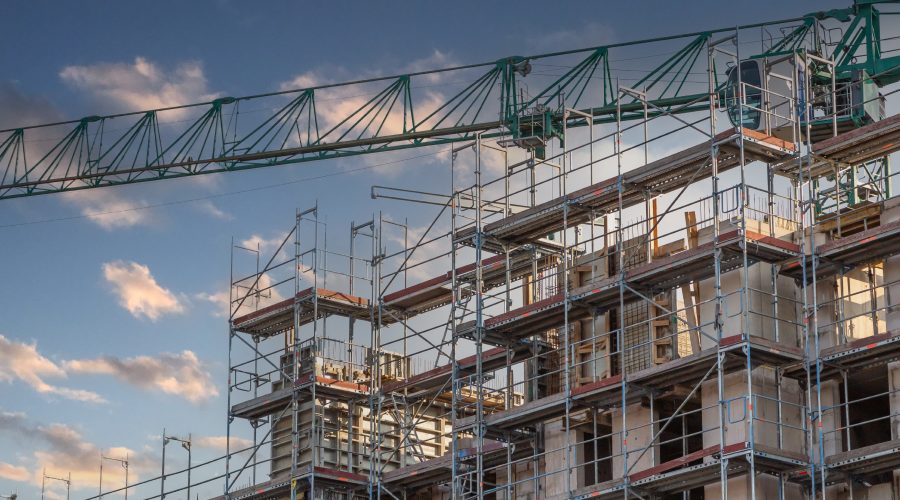 Scaffolding and a tower crane surround a mid-rise apartment building under construction in Germany, symbolizing the country’s stalled construction industry in 2025 amid soaring costs, higher mortgage rates, and shrinking housing permits.