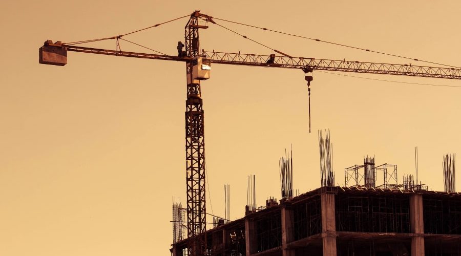 A silhouetted construction crane and partially built structure stand against a golden sunset, symbolizing the construction industry's challenges and transformations. The image conveys resilience and progress, fitting for the topic of how immigration and tariff policies impact the construction sector.