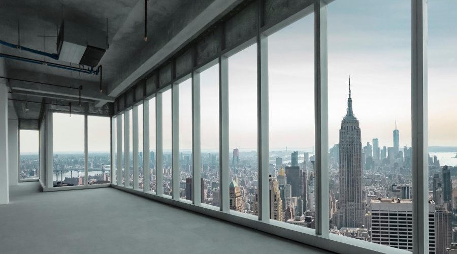 A spacious, unfinished high-rise office with floor-to-ceiling windows overlooking the New York City skyline, including the Empire State Building. The modern, open-floor space reflects the growing demand for premium office real estate, highlighting the opportunities for AEC leaders in the evolving high-end office market.