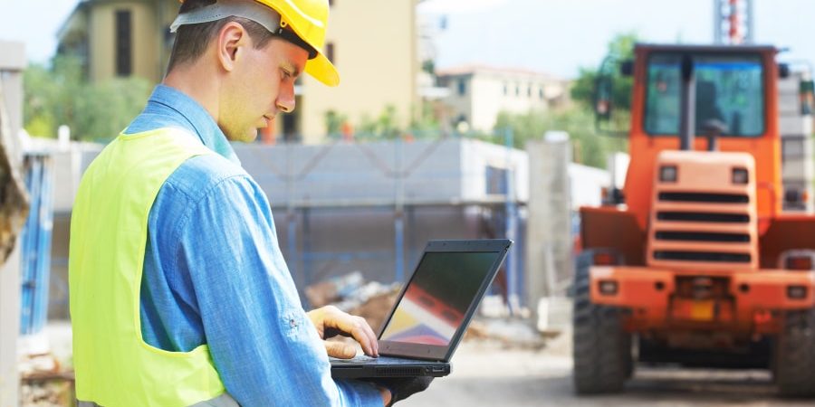 Construction engineer using a laptop at a job site, showcasing the role of digital technology and open data standards in modern infrastructure projects. The future of infrastructure tech relies on seamless data integration for improved collaboration and efficiency.