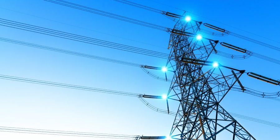 High-voltage power lines on a steel transmission tower at sunset, symbolizing the infrastructure challenges—like copper supply, concrete demand, and permitting delays—that threaten to bottleneck AI expansion.