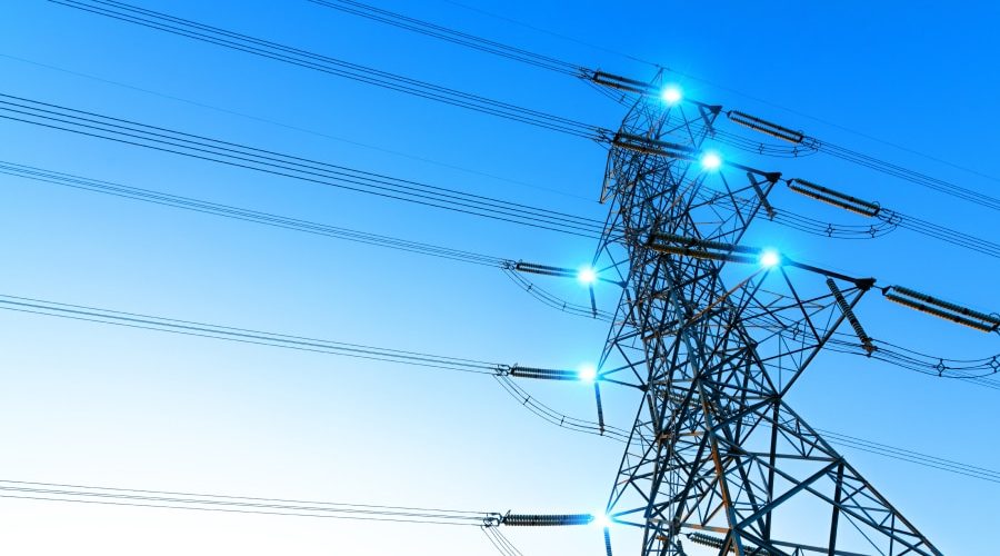 High-voltage power lines on a steel transmission tower at sunset, symbolizing the infrastructure challenges—like copper supply, concrete demand, and permitting delays—that threaten to bottleneck AI expansion.