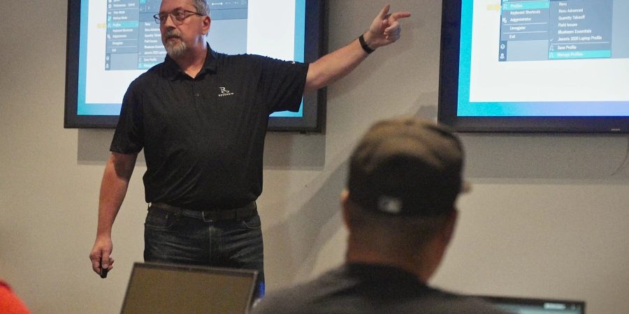 Jason McCarty leads a hands-on Bluebeam training session for electricians, highlighting essential digital tools and leadership skills for success in the field. Two large screens display Bluebeam interface instructions, reinforcing the impact of technology and professional development in the electrical industry.