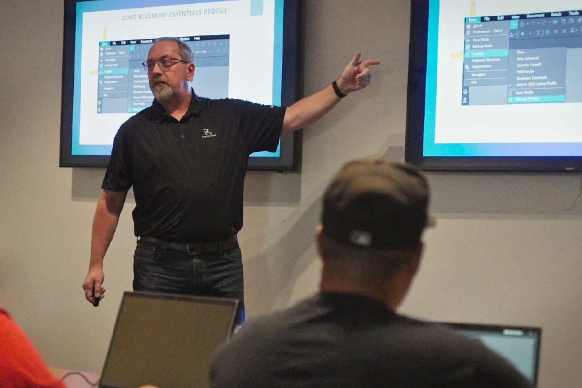 Jason McCarty leads a hands-on Bluebeam training session for electricians, highlighting essential digital tools and leadership skills for success in the field. Two large screens display Bluebeam interface instructions, reinforcing the impact of technology and professional development in the electrical industry.