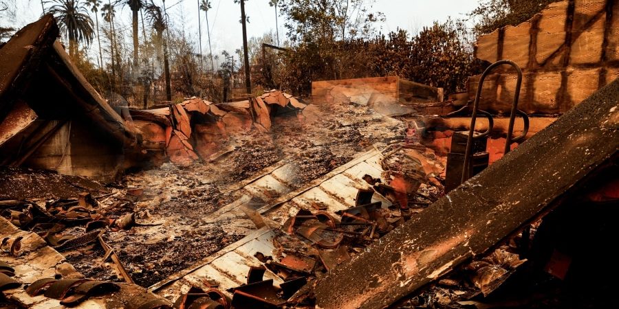 Burned remains of a home after a devastating urban wildfire, with smoldering debris and charred structures. The article 'Urban Wildfire Cleanup: Challenges, Lessons, and How Construction Can Build Resilient Communities' explores recovery efforts, sustainable rebuilding, and fire-resistant construction strategies