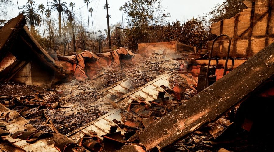 Burned remains of a home after a devastating urban wildfire, with smoldering debris and charred structures. The article 'Urban Wildfire Cleanup: Challenges, Lessons, and How Construction Can Build Resilient Communities' explores recovery efforts, sustainable rebuilding, and fire-resistant construction strategies