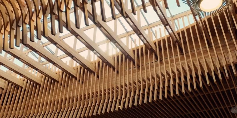 Modern timber ceiling architecture with curved wooden slats and skylights filtering natural daylight, showcasing sustainable mass timber design in a large public interior space.