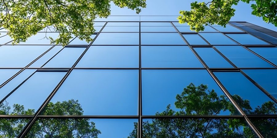 Modern glass building reflecting trees and blue sky, symbolizing sustainable architecture and the environmental transparency promoted by Environmental Product Declarations (EPDs).