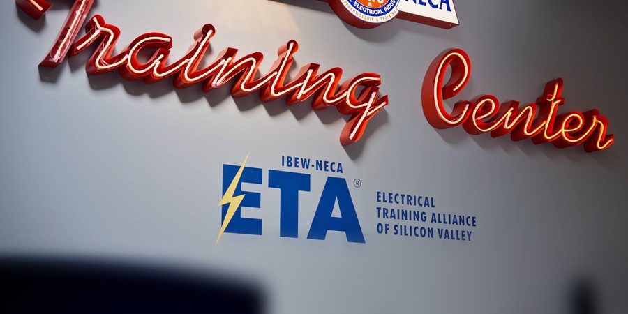 Red neon "Training Center" sign above the IBEW-NECA Electrical Training Alliance of Silicon Valley logo at ETASV in Milpitas, California.