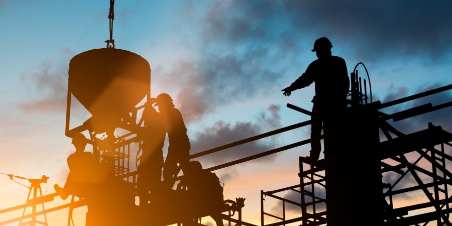 Construction workers silhouetted on a large commercial jobsite at dusk, illustrating the 2026 construction labor shortage and the efficiency mandate facing megaprojects and skilled trades.