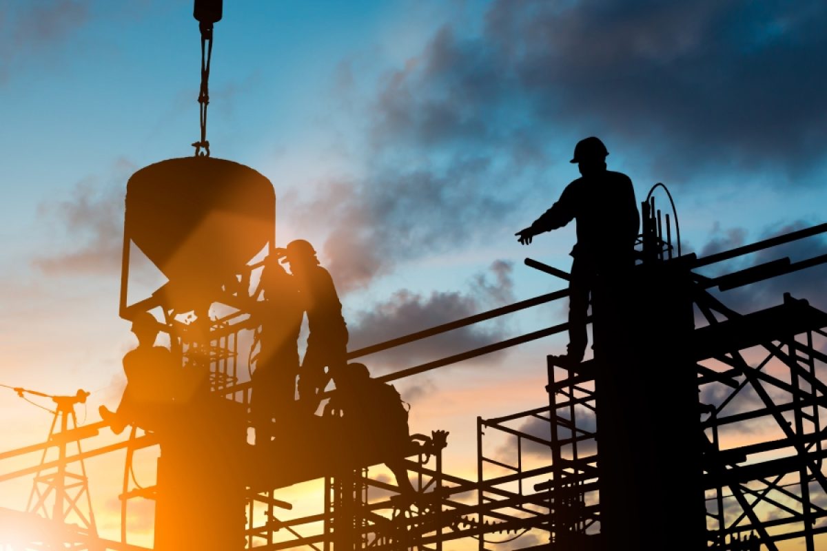 Construction workers silhouetted on a large commercial jobsite at dusk, illustrating the 2026 construction labor shortage and the efficiency mandate facing megaprojects and skilled trades.