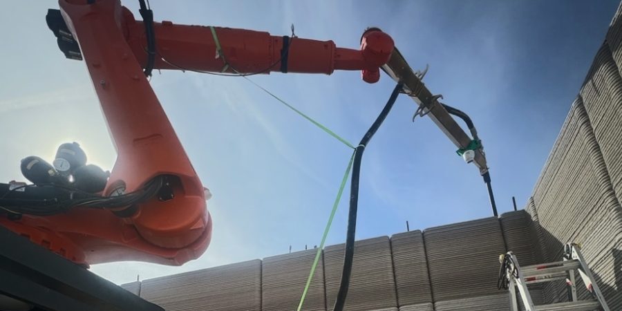RIC robotics_900x600_24 Robotic 3D printer RIC-PRIMUS pouring concrete walls for a big-box retail store under blue sky, demonstrating how construction robots cut labor and build time to finish warehouses in just seven days.