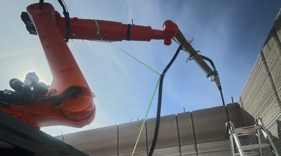 Robotic 3D printer RIC-PRIMUS pouring concrete walls for a big-box retail store under blue sky, demonstrating how construction robots cut labor and build time to finish warehouses in just seven days.