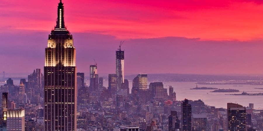 A dramatic sunset over Manhattan highlights the Empire State Building and One World Trade Center—two iconic symbols of American resilience, innovation, and ambition—representing megaprojects that shaped U.S. infrastructure and identity.