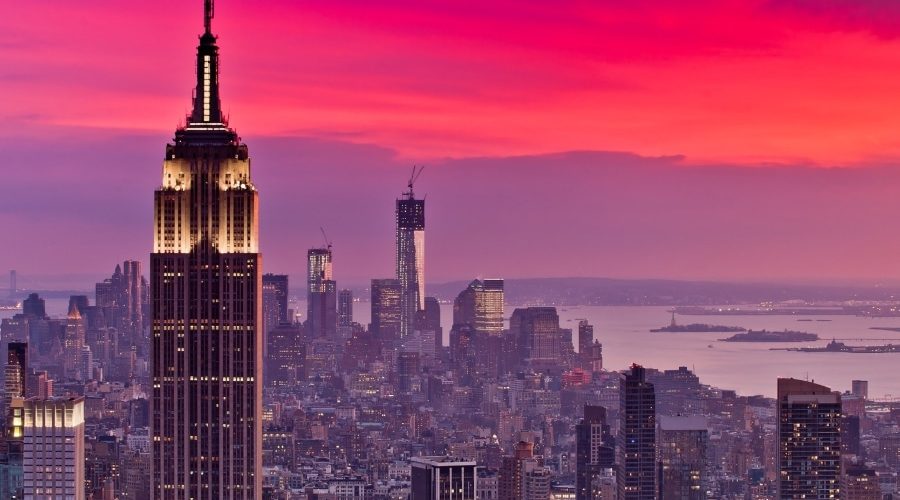 A dramatic sunset over Manhattan highlights the Empire State Building and One World Trade Center—two iconic symbols of American resilience, innovation, and ambition—representing megaprojects that shaped U.S. infrastructure and identity.