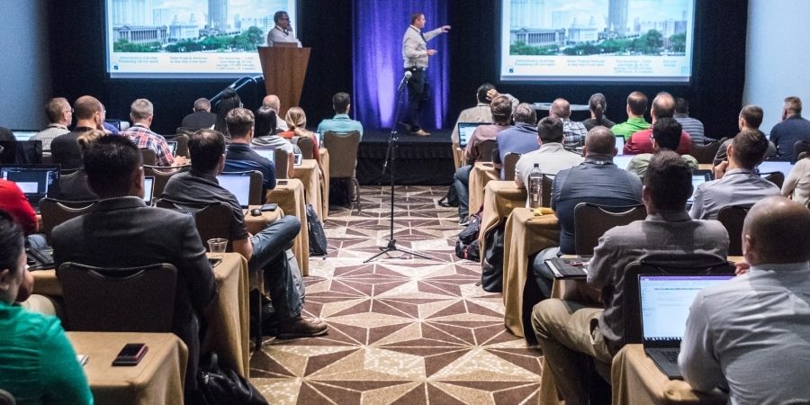 Attendees at a Bluebeam Unbound conference session watch a case study presentation in a packed room with laptops open, highlighting key sessions and industry insights.