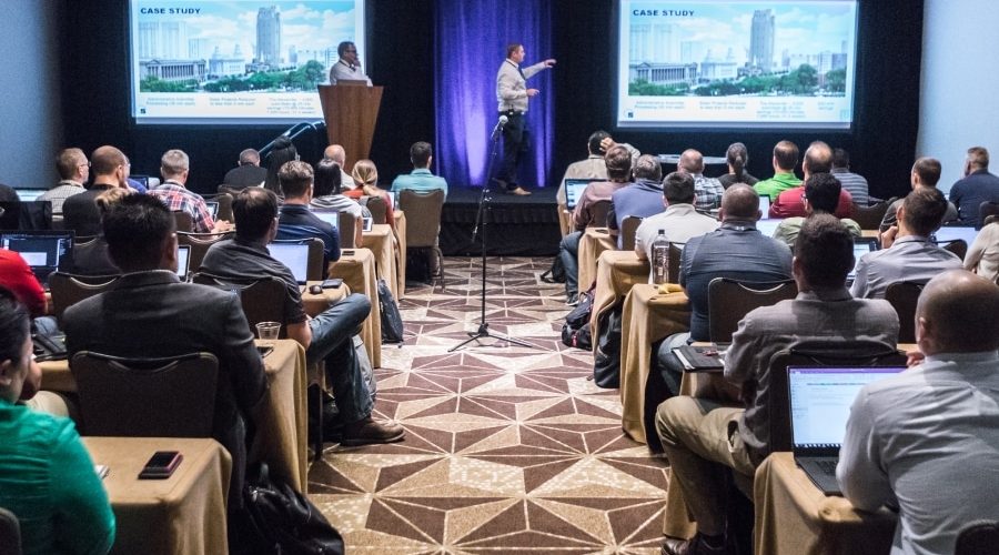Attendees at a Bluebeam Unbound conference session watch a case study presentation in a packed room with laptops open, highlighting key sessions and industry insights.