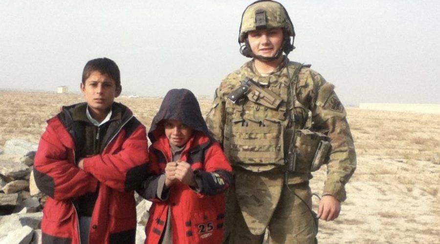 Josh Sergent, in full U.S. Air Force combat gear, stands with two local Afghan children wearing red jackets during a patrol mission, symbolizing his service abroad before transitioning into a career in construction and customer success at Bluebeam.