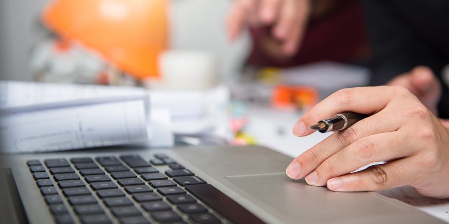 Estimator reviewing revised construction drawings and performing digital takeoff on laptop in jobsite trailer during project revision.