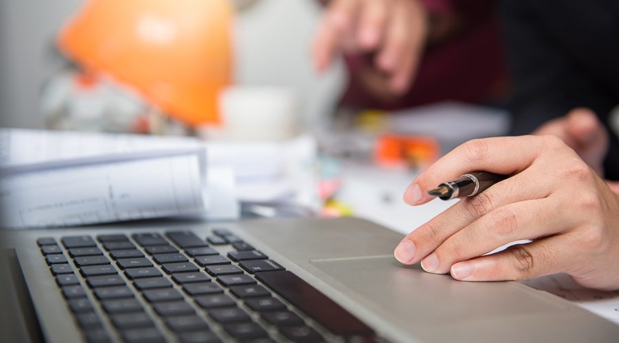 Estimator reviewing revised construction drawings and performing digital takeoff on laptop in jobsite trailer during project revision.