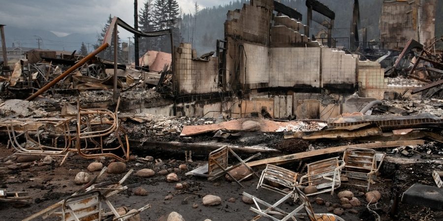 Burned residential structures and debris after a wildfire, showing cleared lots and stalled rebuilding in an urban neighborhood during post-fire recovery.